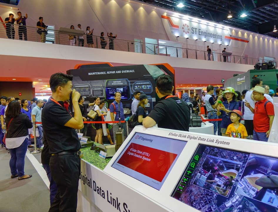 Interactive exhibition booth showcasing digital data link systems and maintenance technology at a crowded trade show event